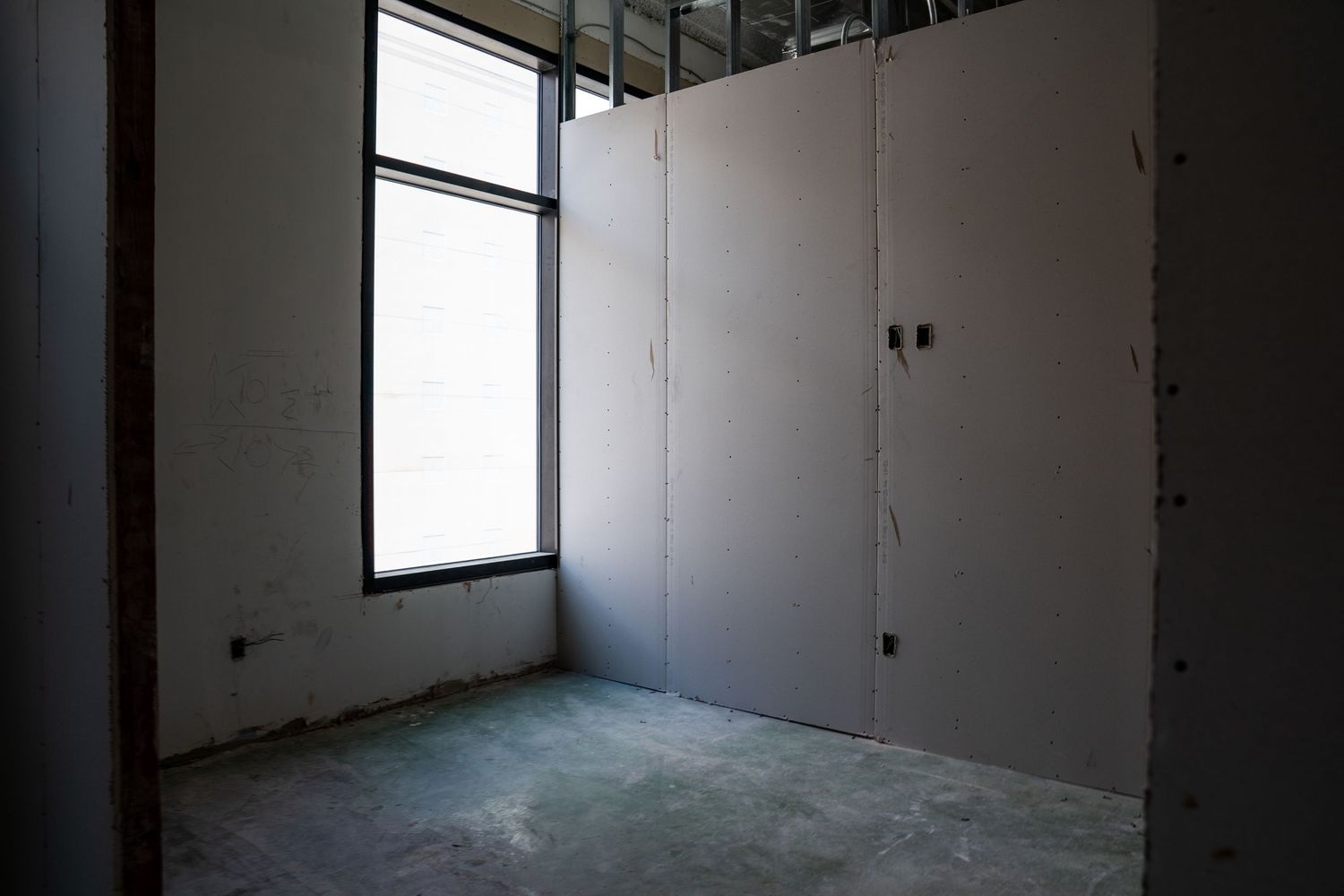 An empty room with white walls, concrete floor, and a large window during construction.