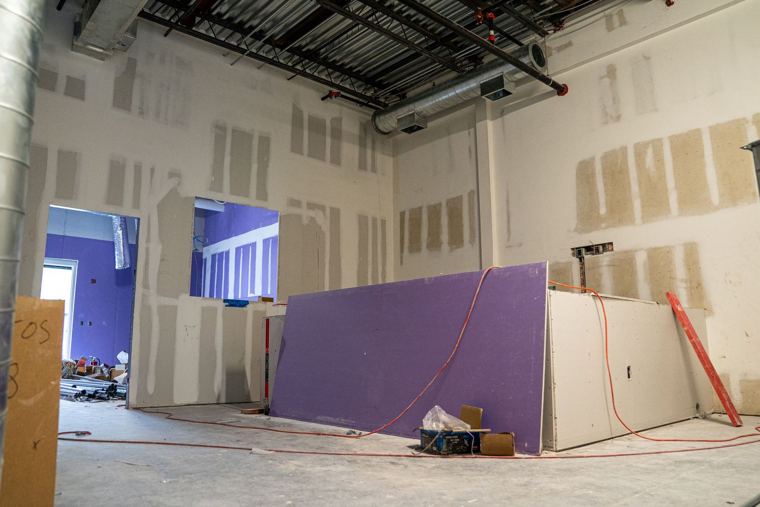 Construction area with purple partition wall and exposed ceiling infrastructure.