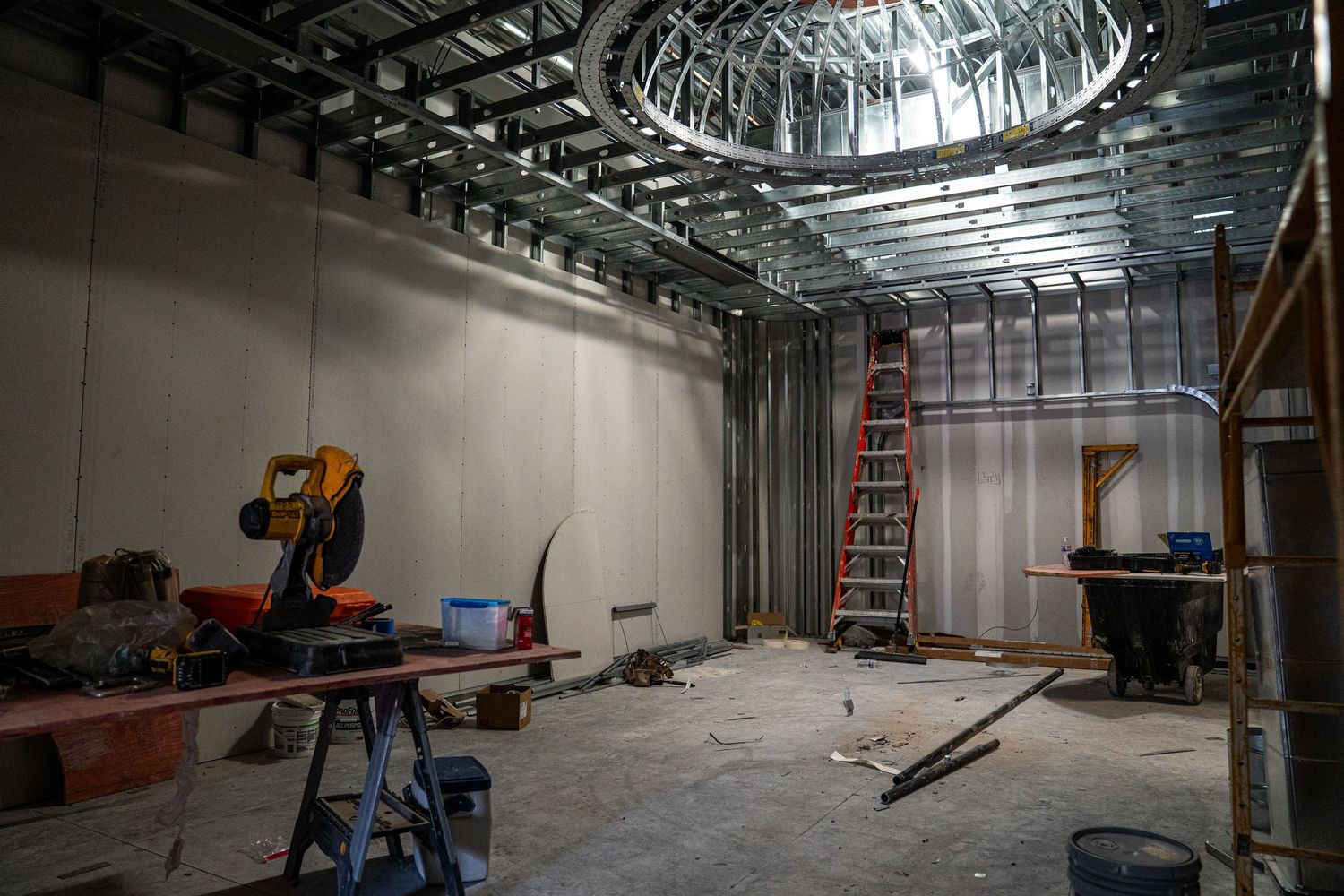 Construction site with circular ceiling feature, orange ladder, and tools scattered throughout unfinished room.