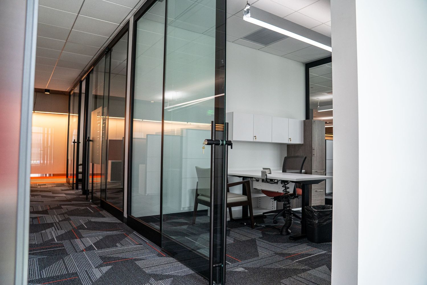 Sleek office corridor with glass-walled meeting rooms and modern workspace furniture.