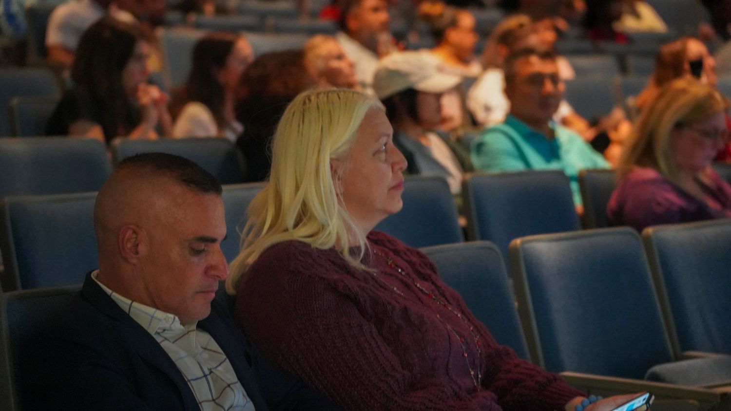 People seated in blue theater chairs watching an event.