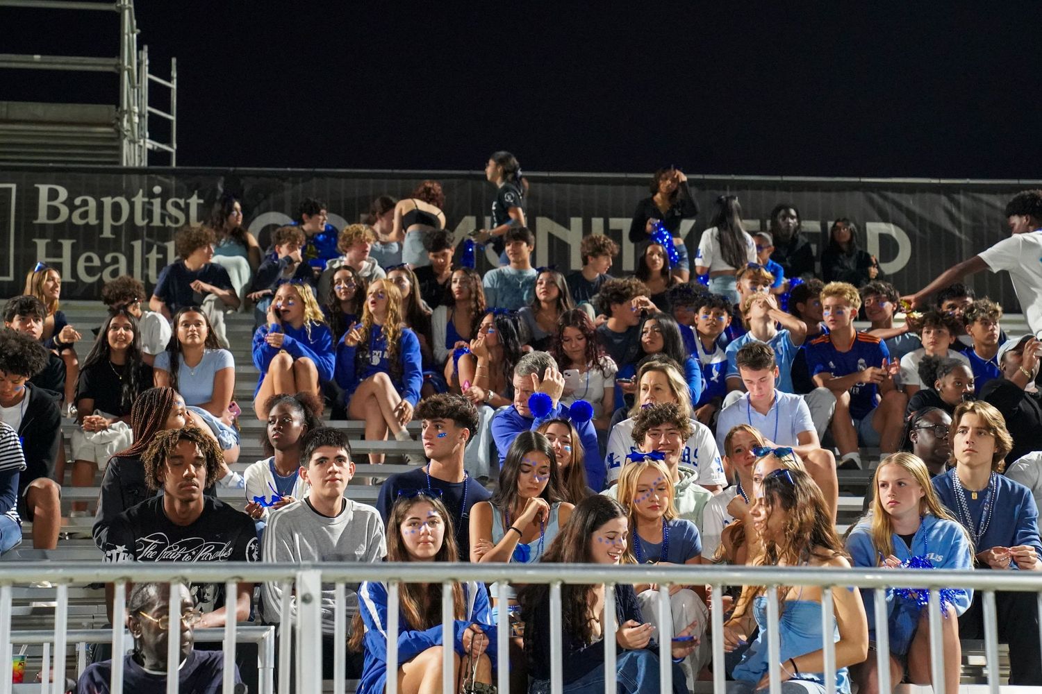Large crowd of students filling stadium bleachers during a nighttime sporting event.