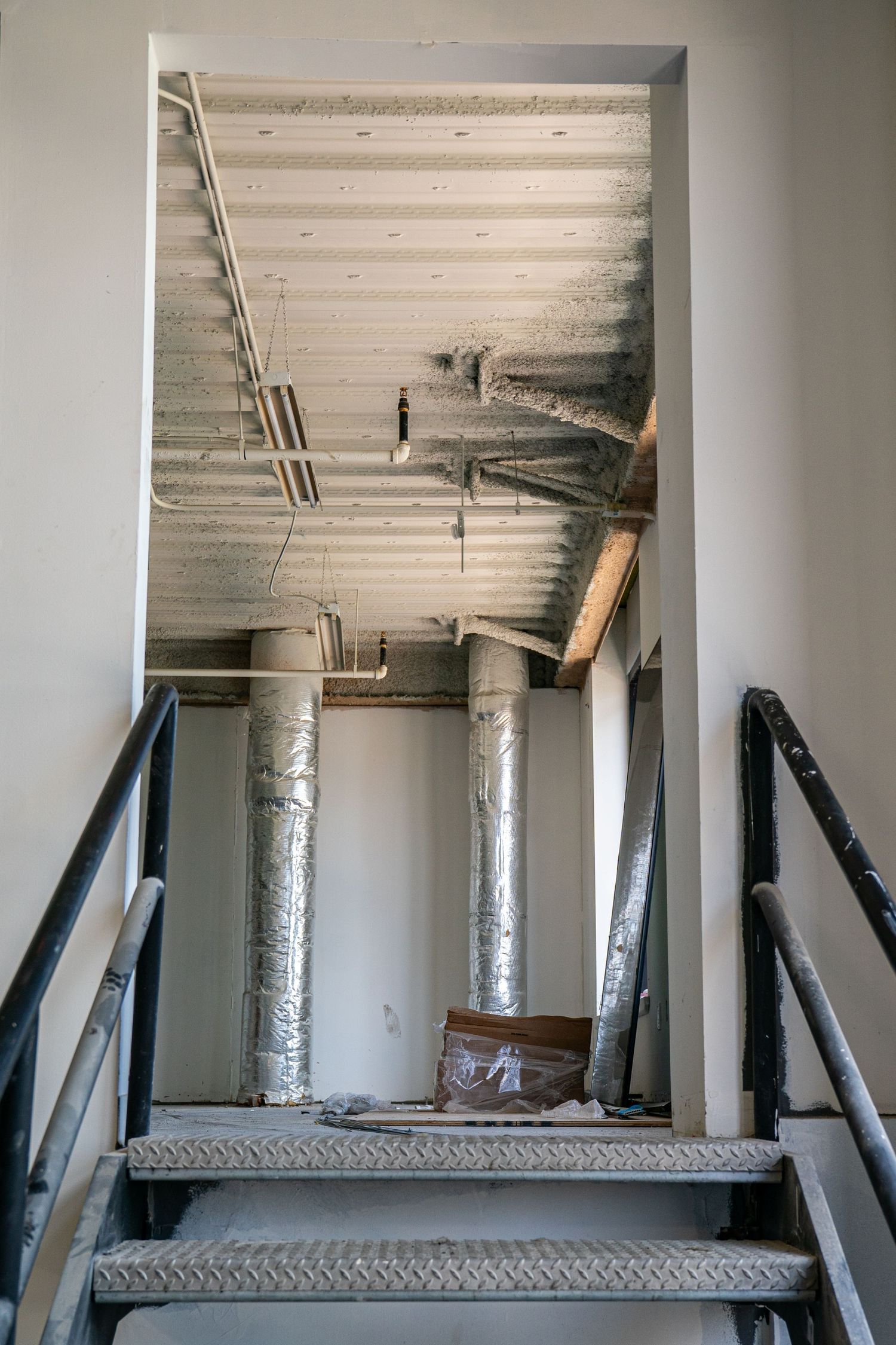 Empty industrial space with white columns and exposed ceiling showing temporary support beams during renovation.