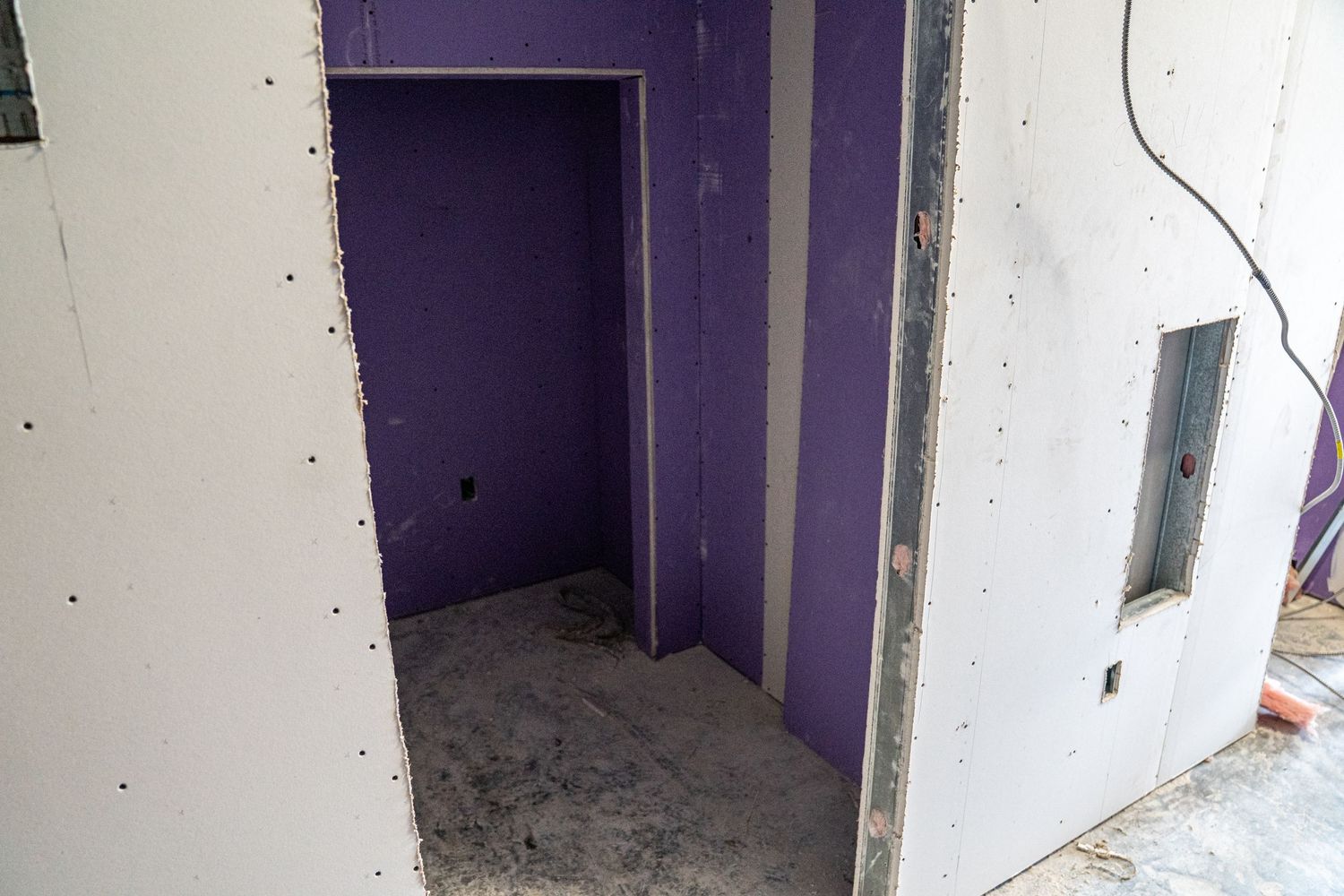 Construction site showing a room with purple walls and unfinished flooring.