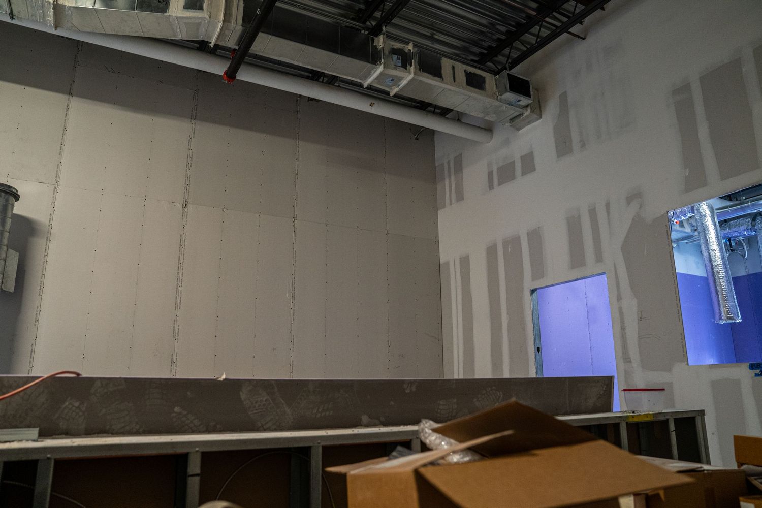 Construction site interior showing unfinished walls and exposed ceiling with metal ductwork and wiring.