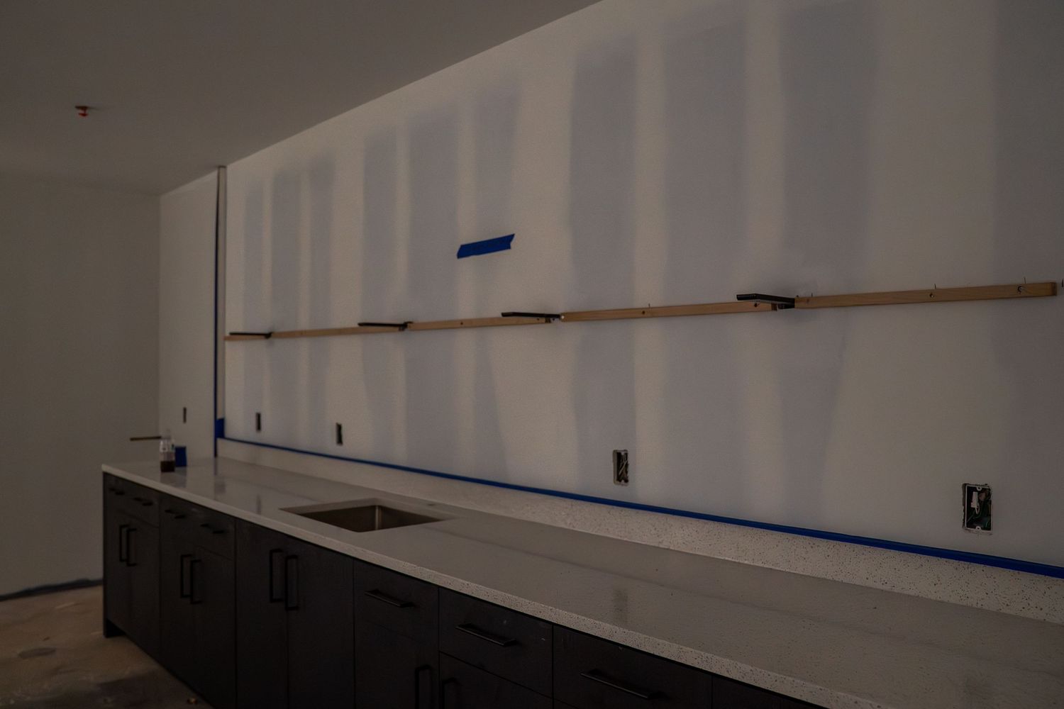 White interior walls with dark baseboards and blue tape markings during renovation.