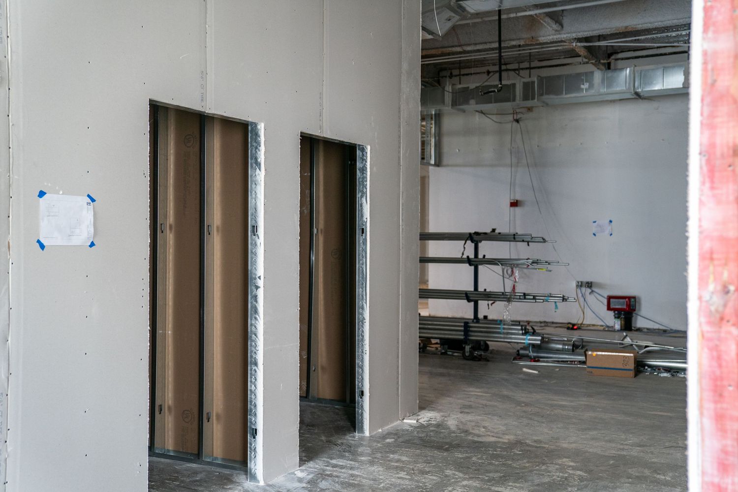 An industrial hallway under construction with brown doors and exposed ceiling infrastructure.