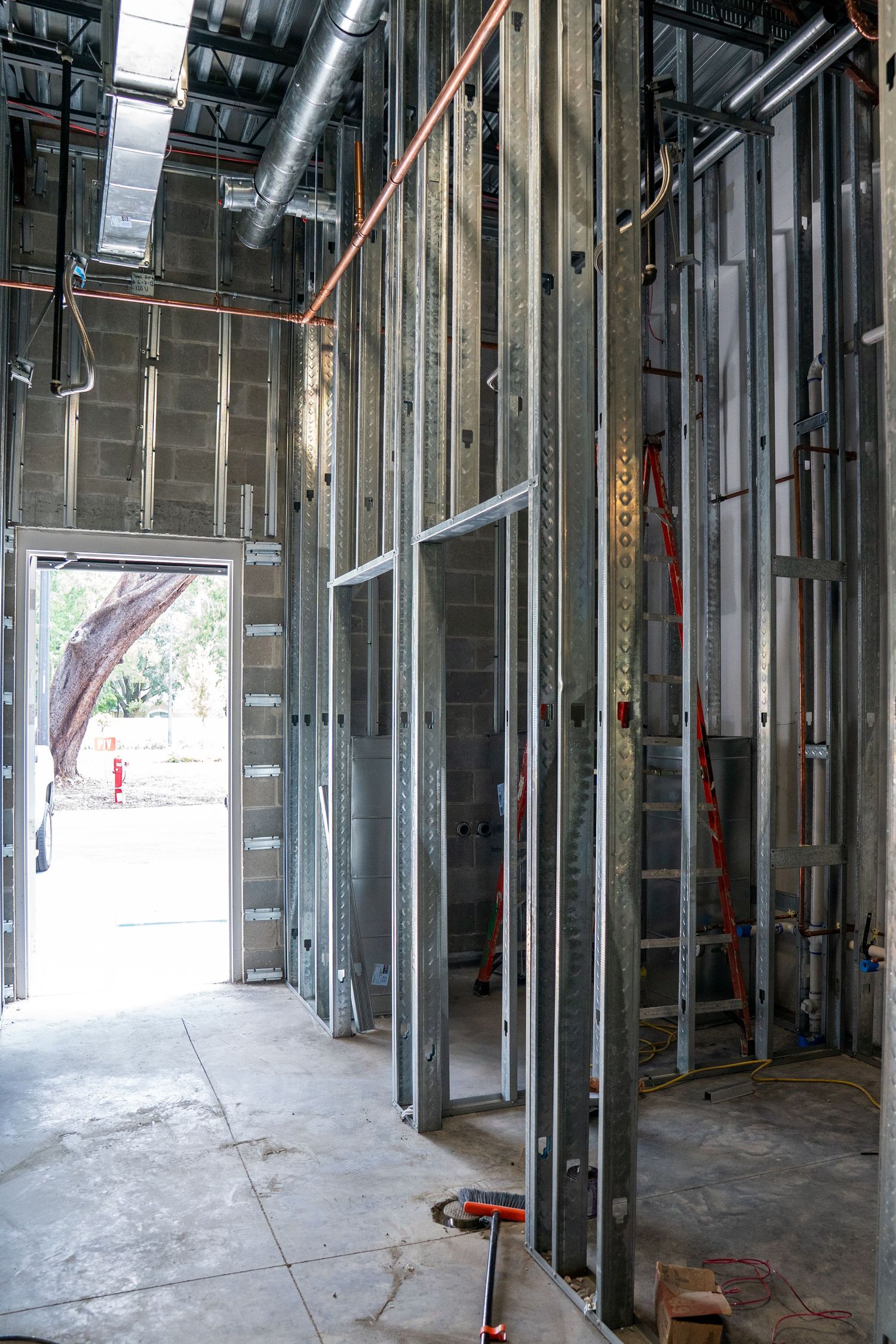 Metal framing and studs line an unfinished commercial space with concrete floors during construction.