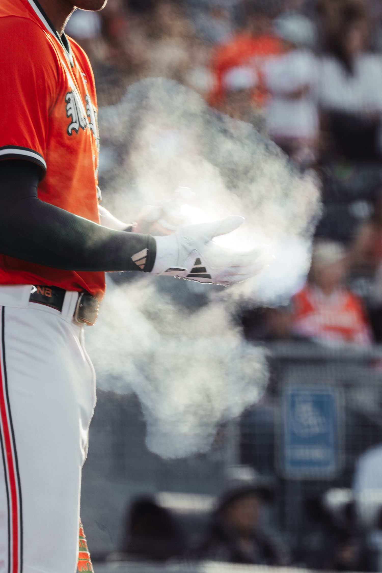 Baseball player in orange uniform clapping hands with chalk dust cloud rising during game preparation.