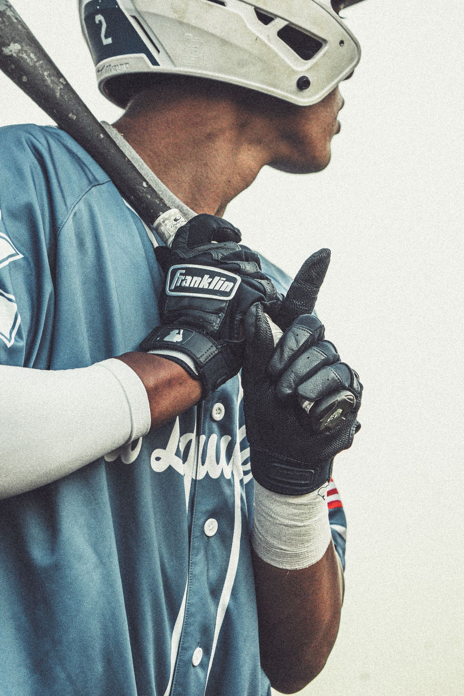 Baseball player in blue jersey and Franklin batting gloves holds bat over shoulder, wearing white helmet with number 2.