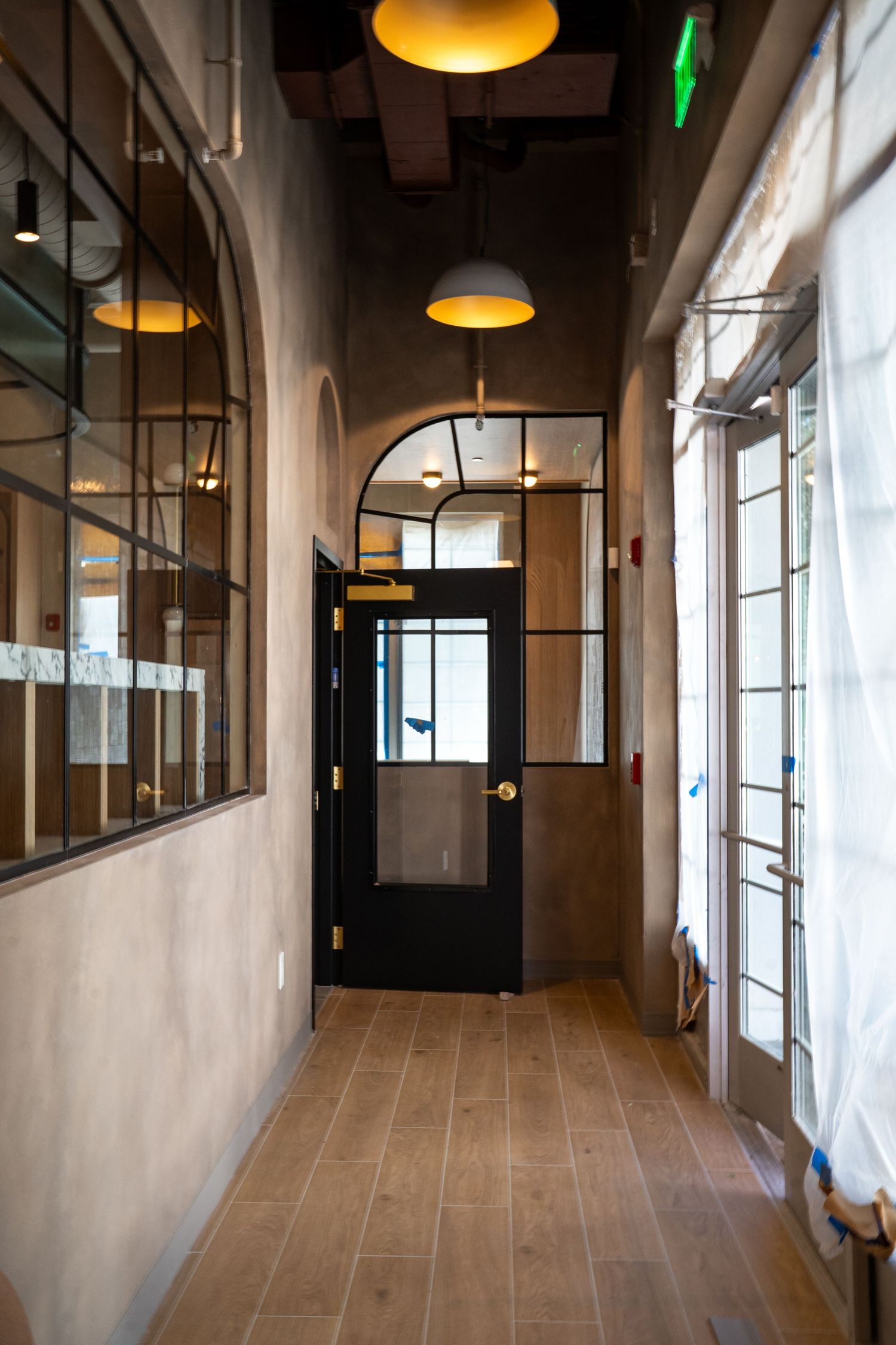 Modern office hallway with industrial pendant lights, glass partitions, and tiled flooring extends into the distance.
