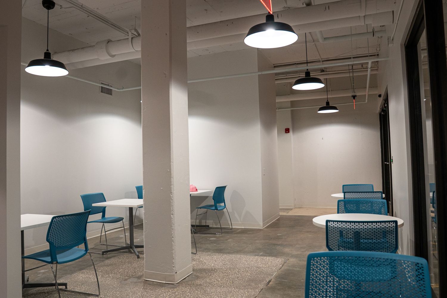 Large empty commercial space under construction with exposed ceiling and blue chairs visible in the distance.