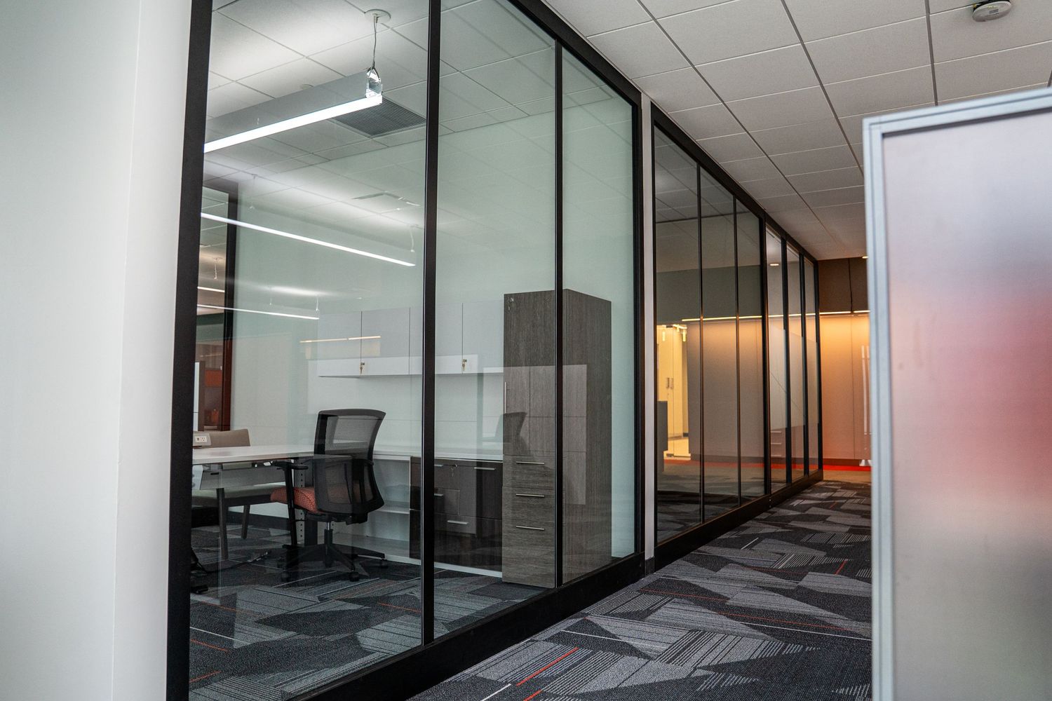 Corporate office hallway with glass-walled meeting rooms and modern carpet design.