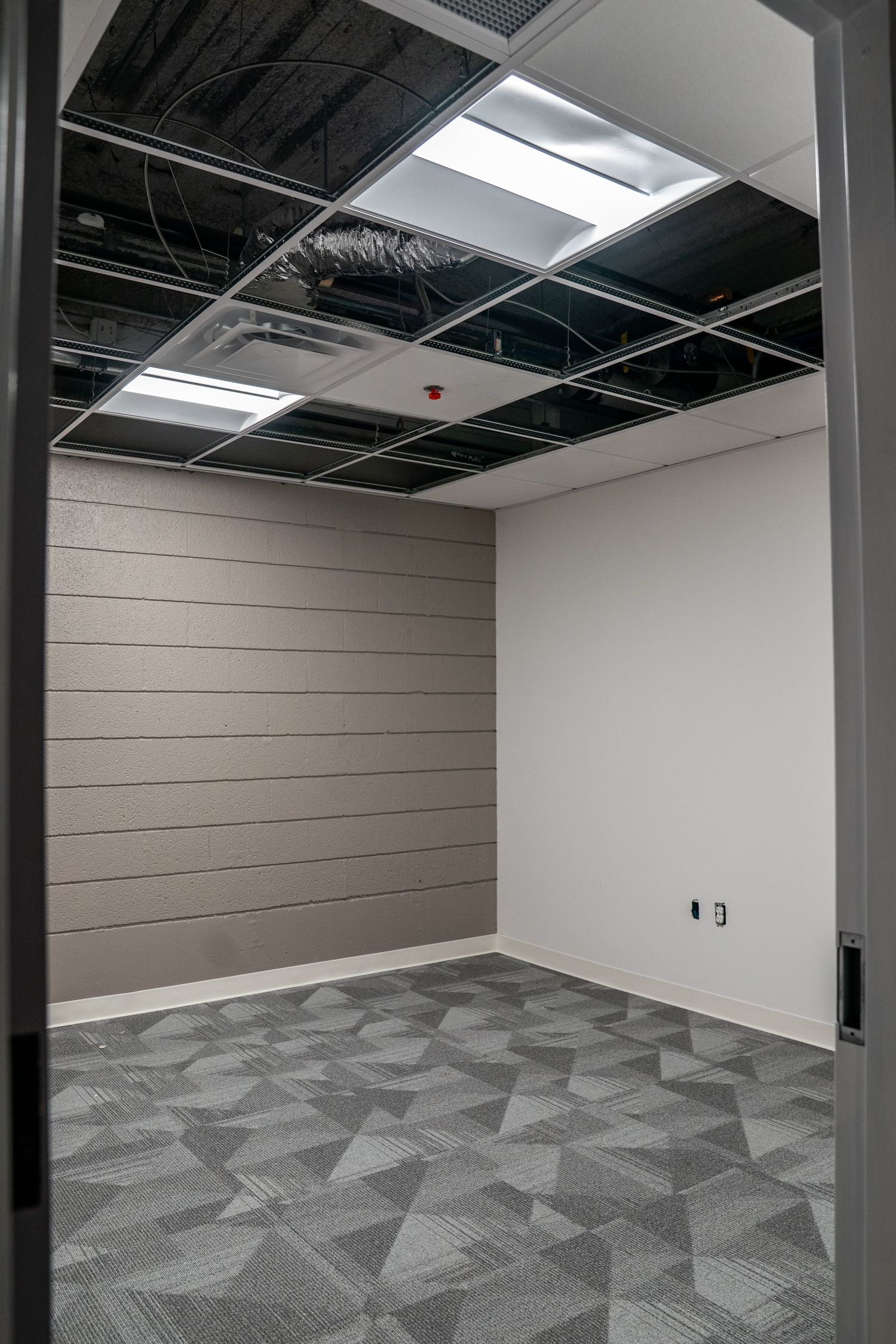 Empty commercial space with geometric patterned carpet and exposed ceiling infrastructure.