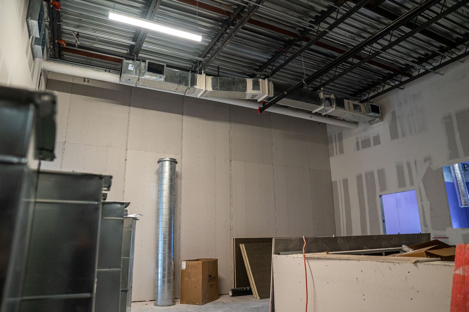 Partially completed commercial interior with exposed ceiling infrastructure and drywall.