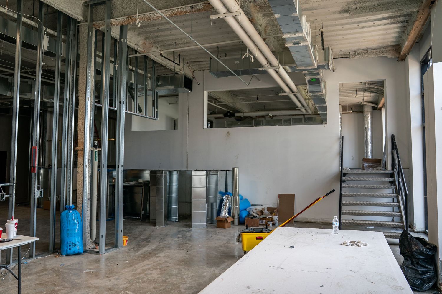 Long view of commercial space under renovation showing metal framing and utility installations.