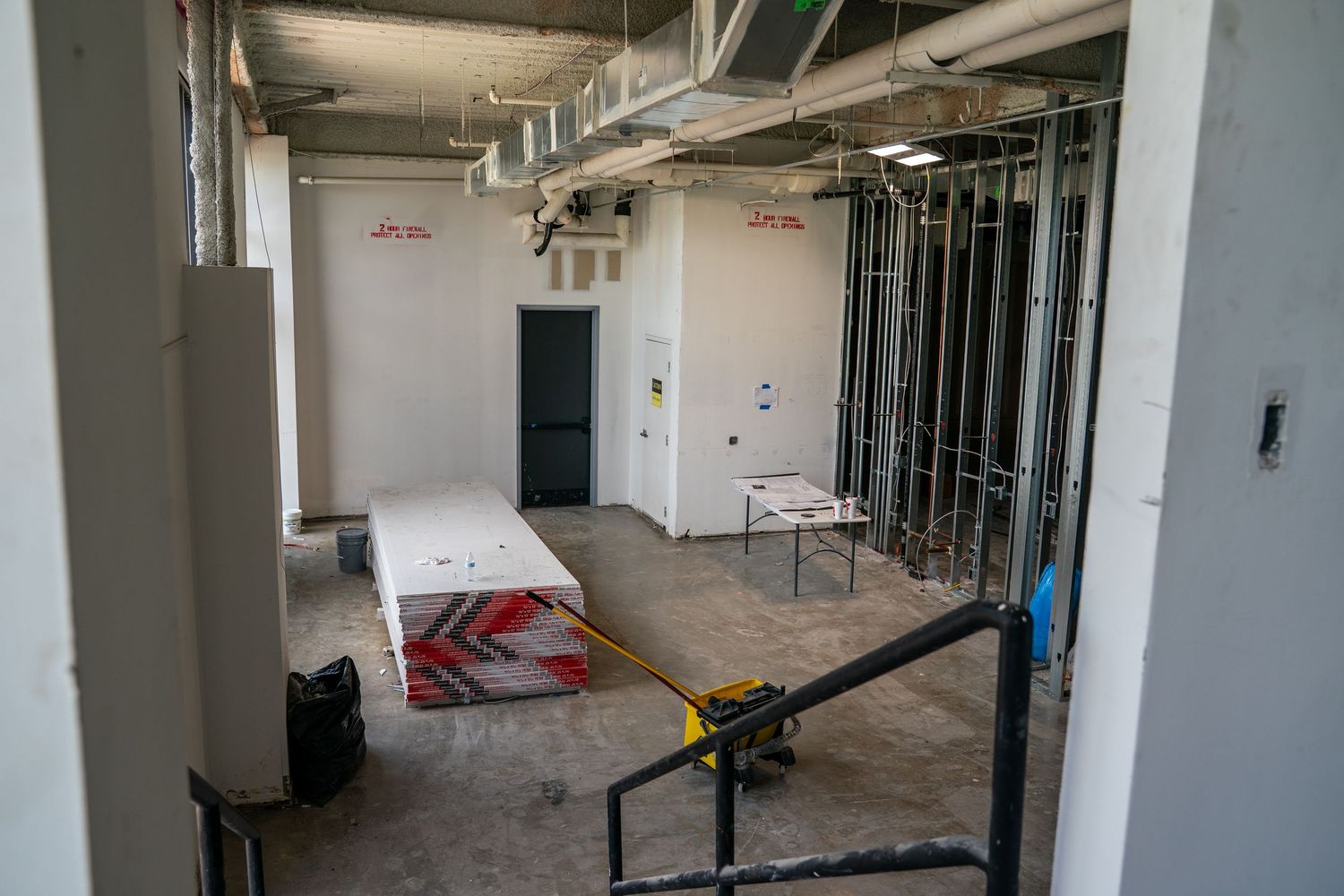 Long empty commercial space with white columns and industrial lighting fixtures.