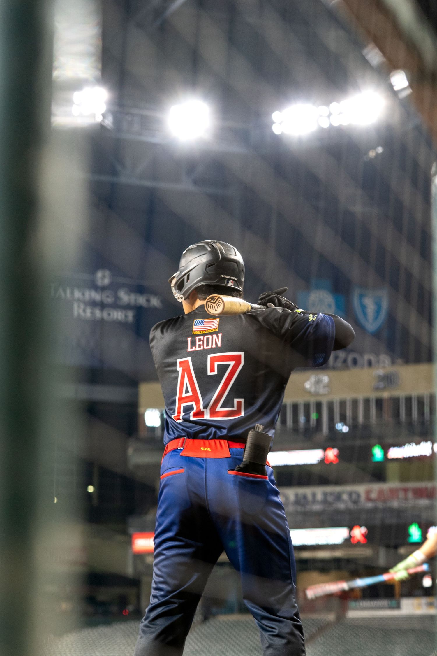 A baseball player swings a bat during a game in a stadium with illuminated lights and signage in the background.