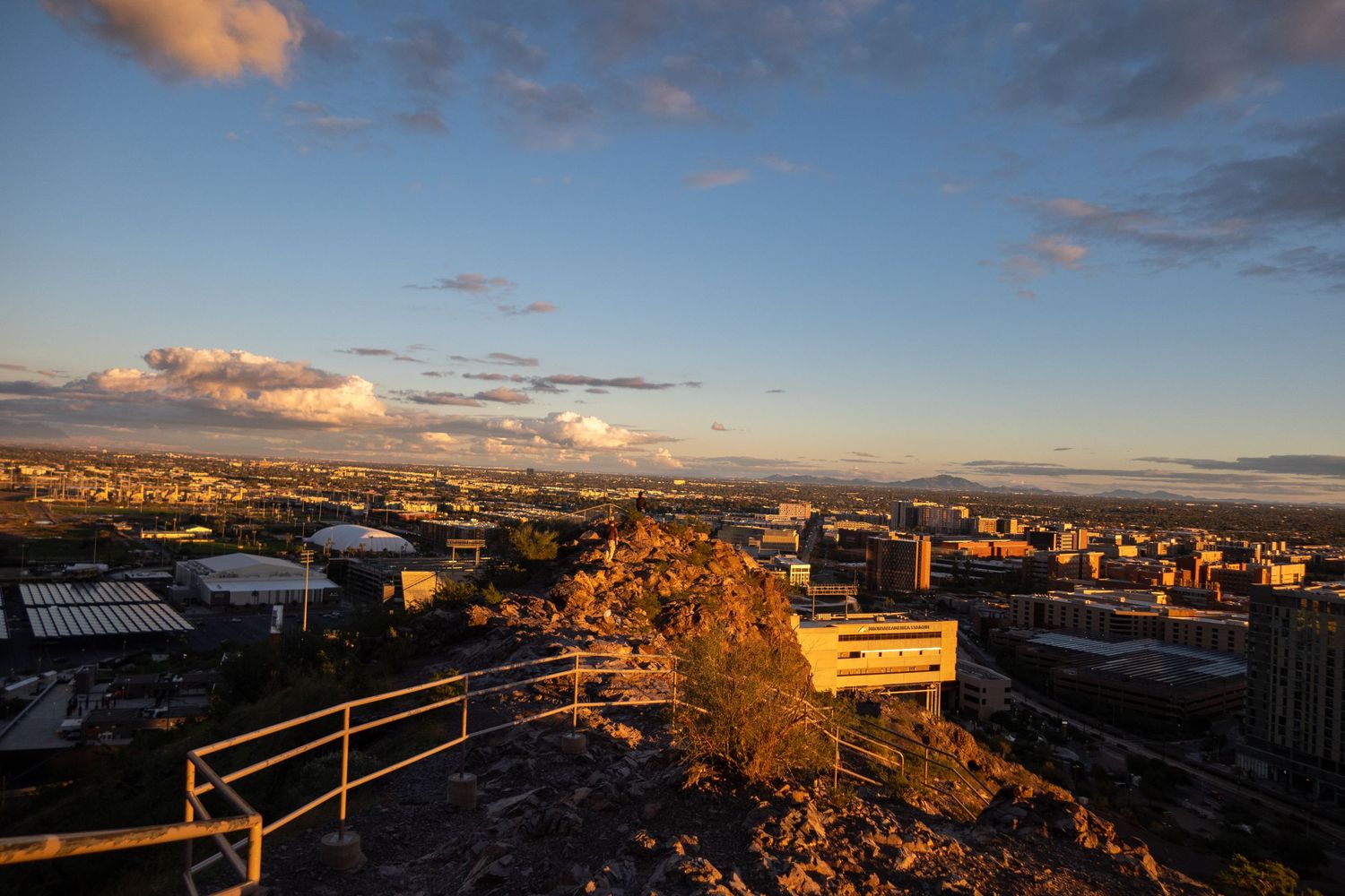 Scenic overlook of city buildings and mountains with warm sunset lighting.