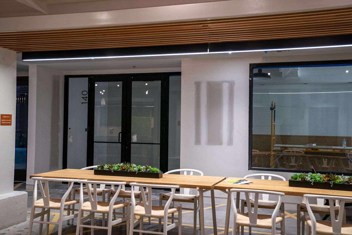 Modern cafeteria space with wooden tables and chairs arranged in neat rows near large windows.