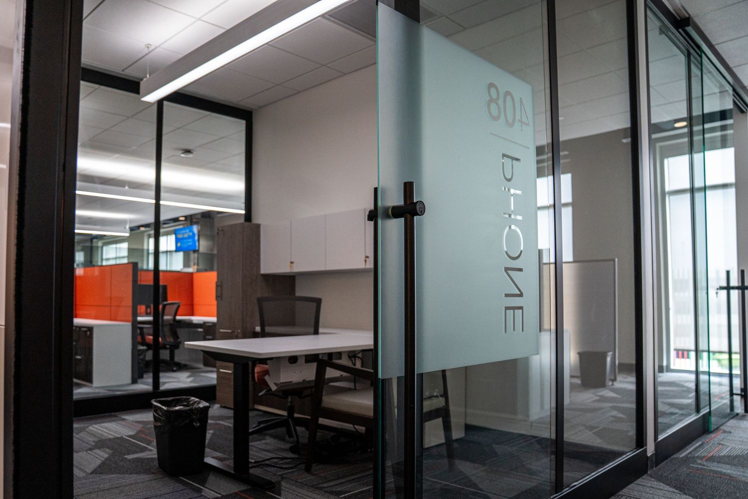 Glass-walled meeting room with modern furniture and orange accents visible through transparent partitions.