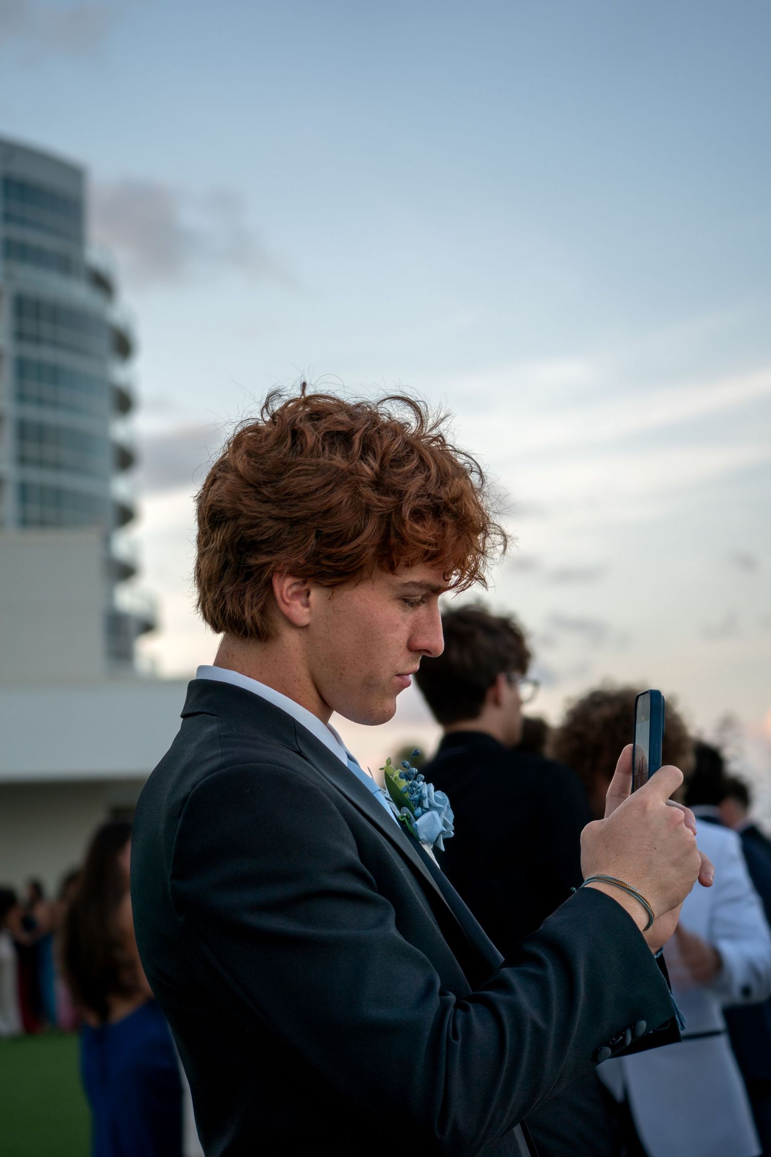 A formal event attendee checks their phone against a twilight sky backdrop.