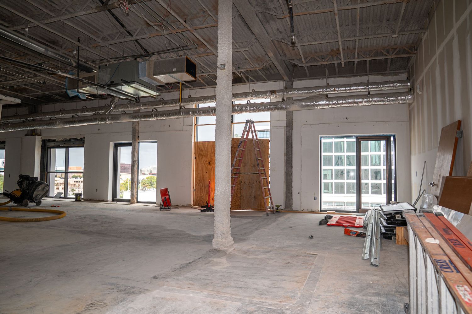 Wide commercial interior space showing support columns and unfinished ceiling during construction phase.