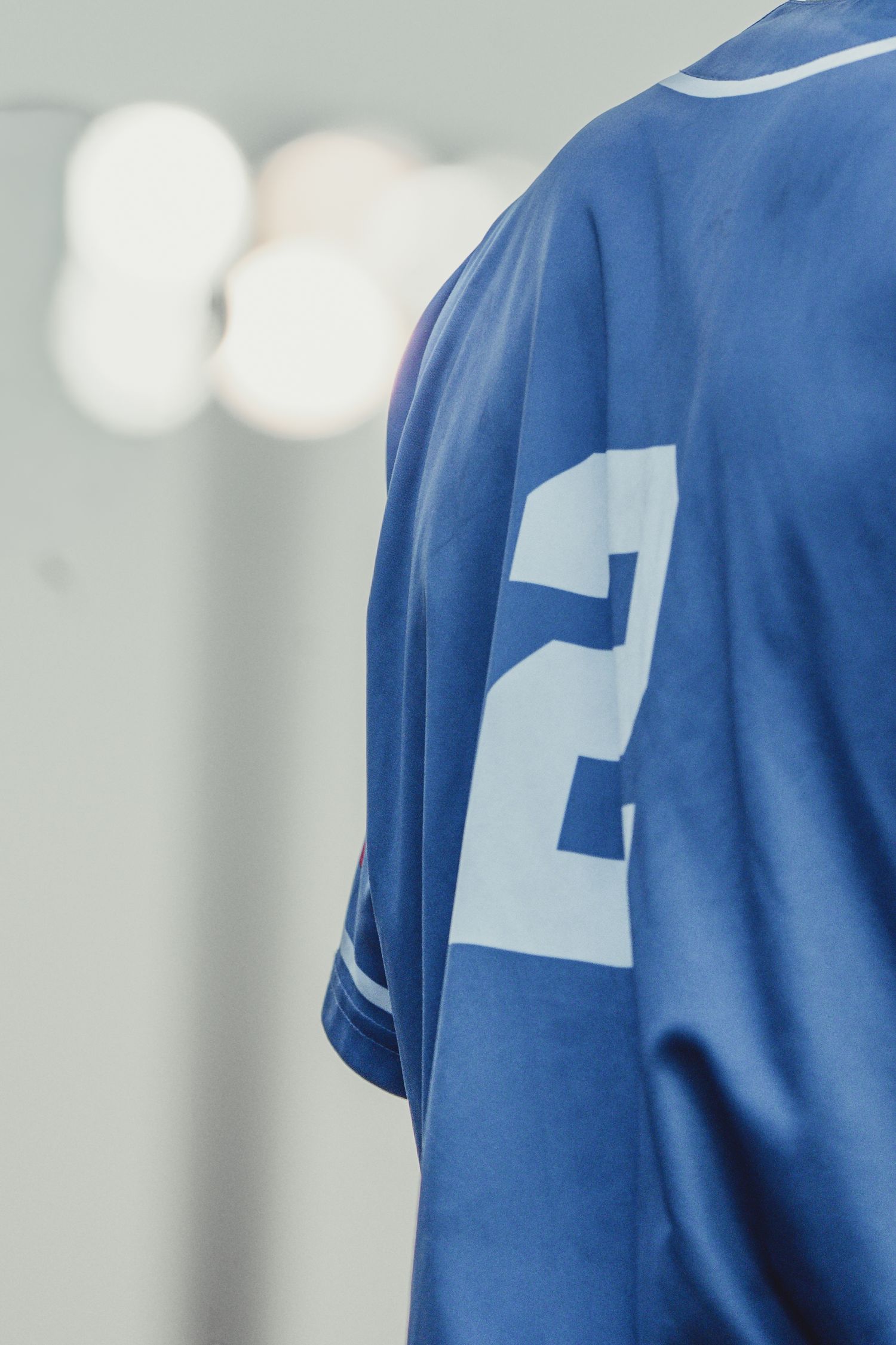 Close-up of a blue sports jersey with the number 2, worn by an athlete in a bright locker room.