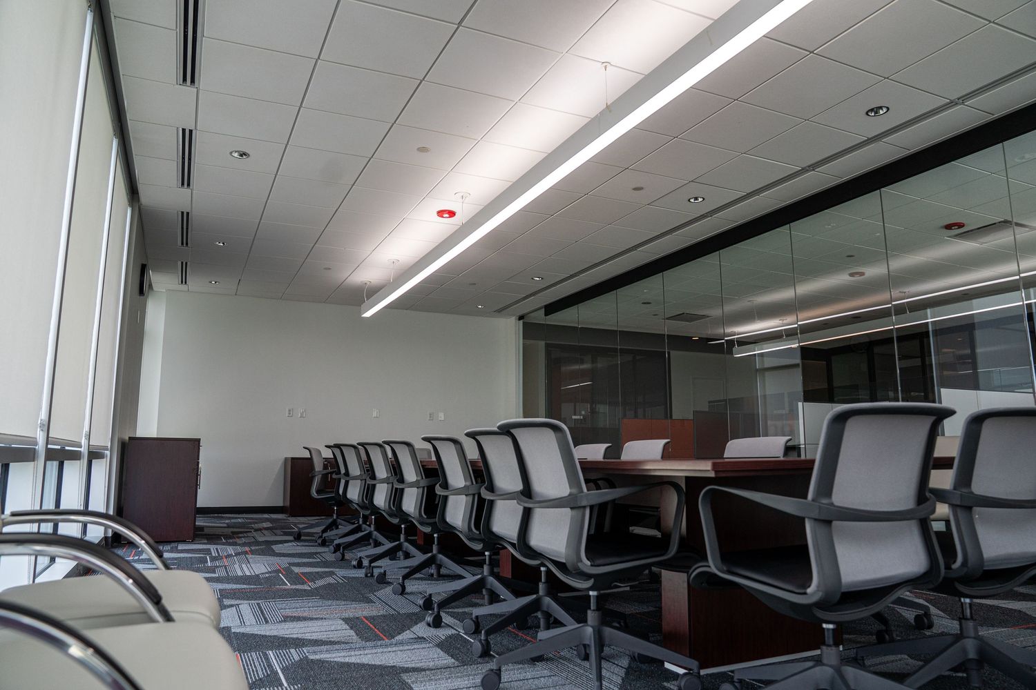 Corporate boardroom with sleek black chairs around mahogany table under linear lighting fixtures.