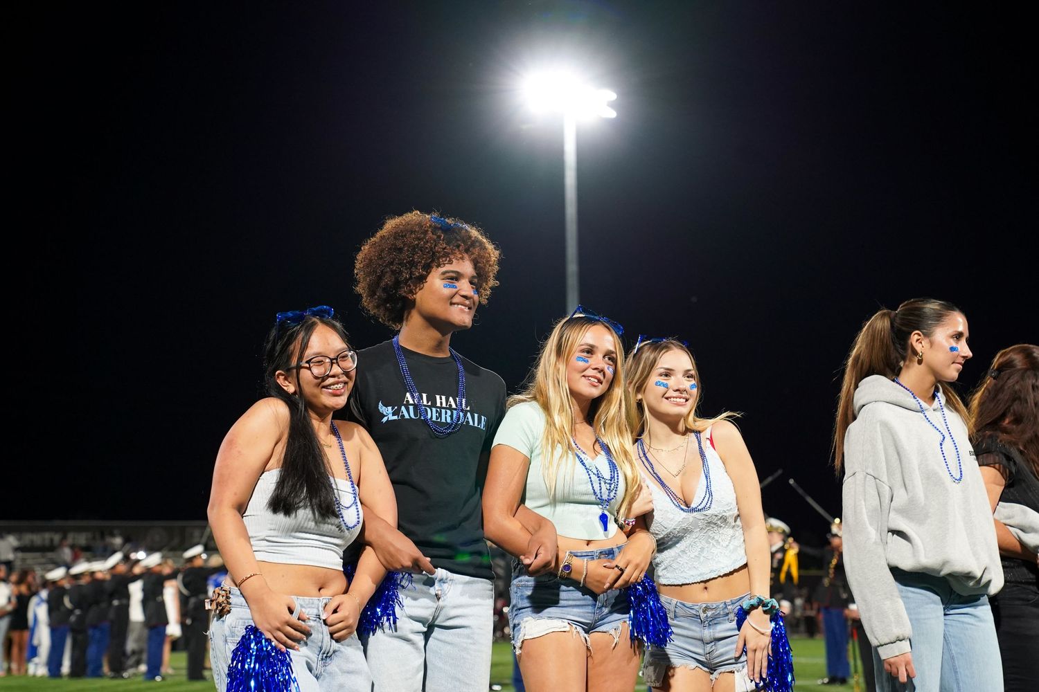 Large group of students stand together on an illuminated field during a nighttime ceremony.
