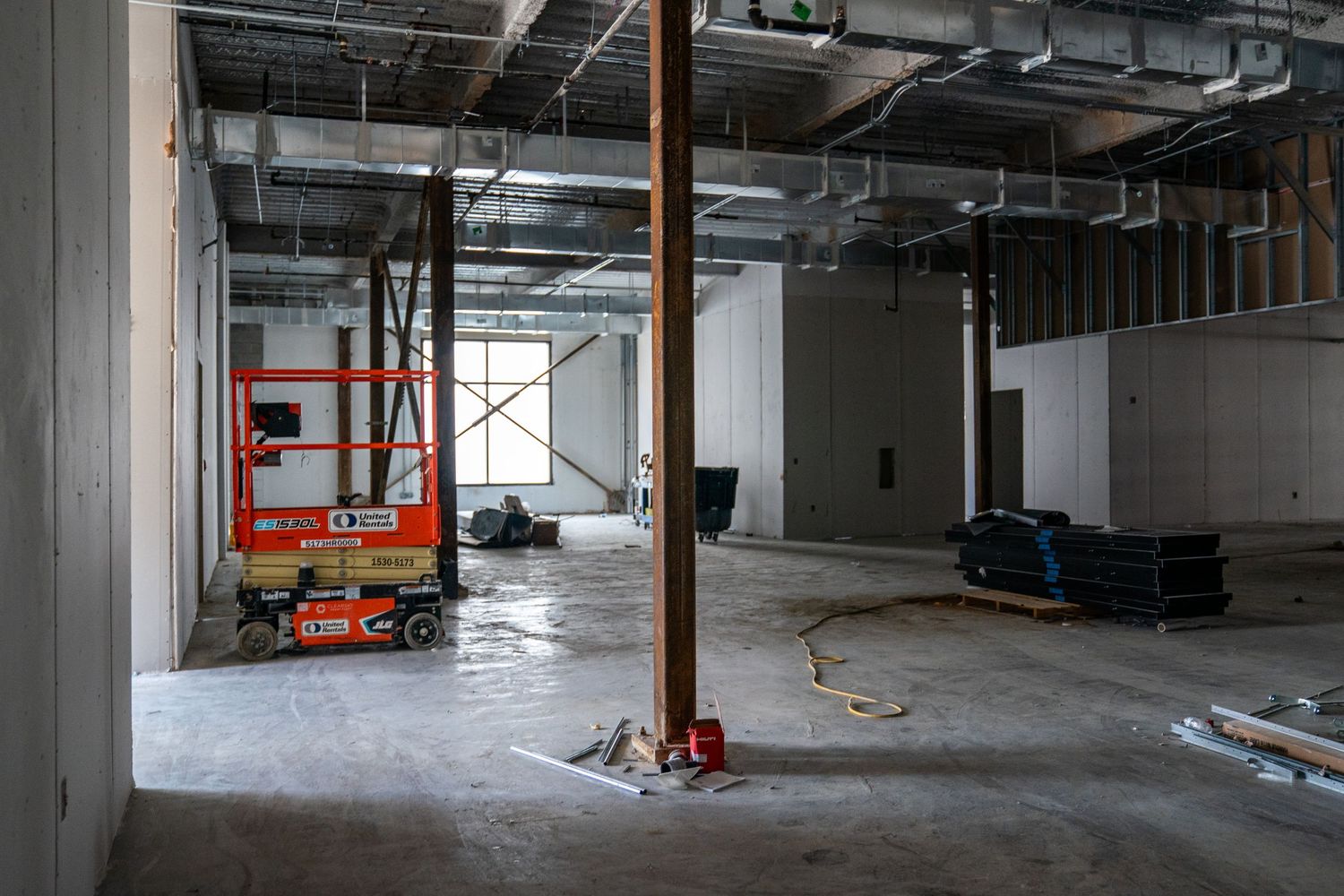 Construction site with scissor lift, support columns, and building materials in an empty commercial space.