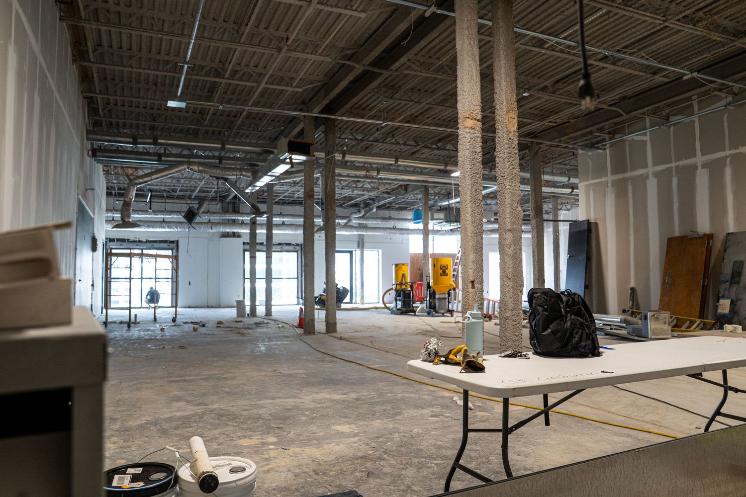 Large open warehouse space during renovation showing exposed ceiling and construction materials.