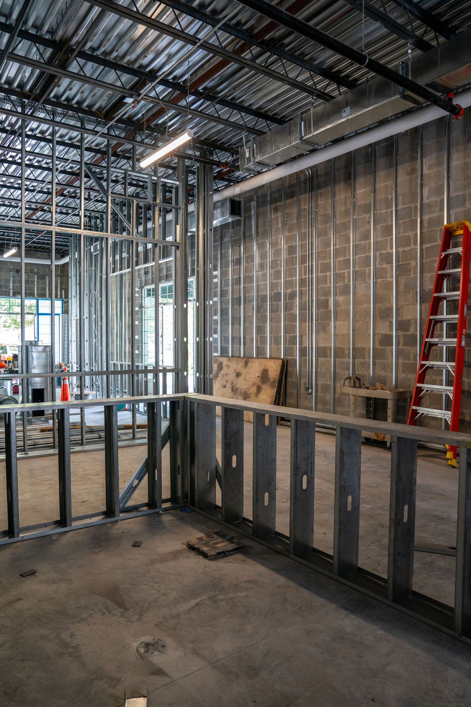 Construction site interior showing metal stud framing and exposed ceiling infrastructure.