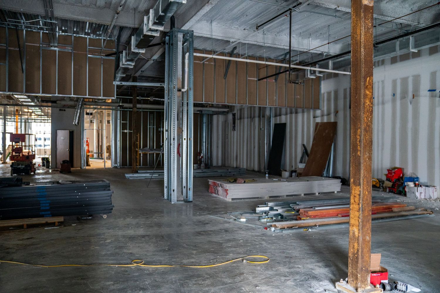Commercial space under renovation with exposed metal framing, ductwork, and construction materials visible.