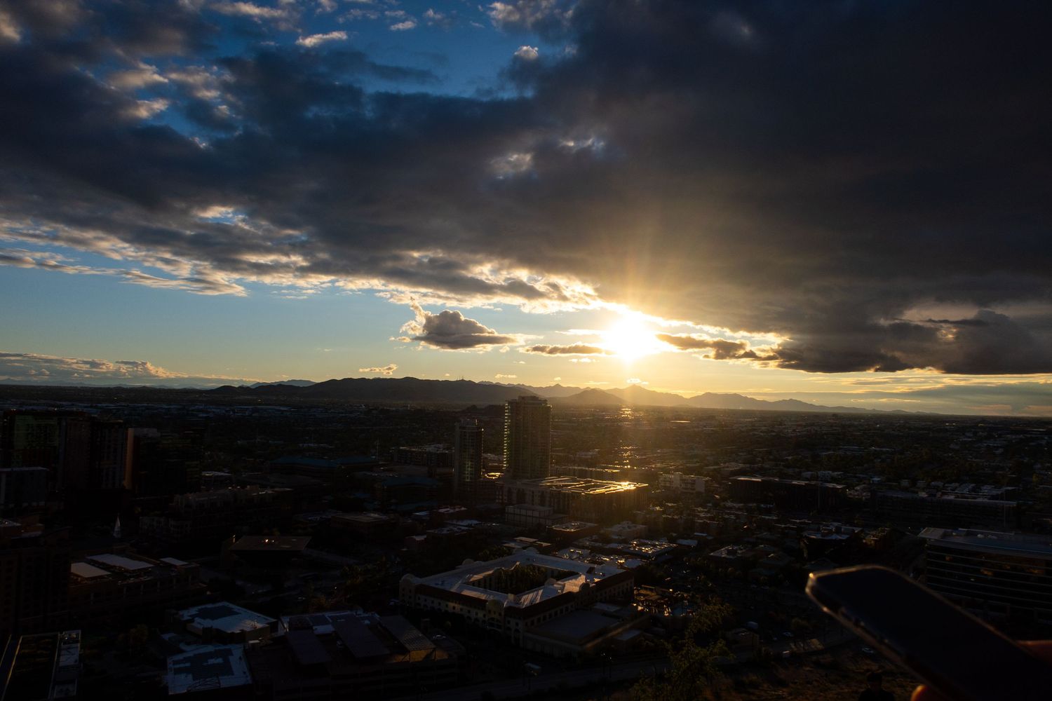 Panoramic view of city under stormy clouds with sunbeams breaking through.