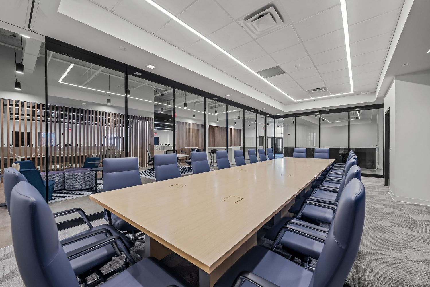 Modern office conference room with blue chairs and long wooden table under sleek lighting fixtures.