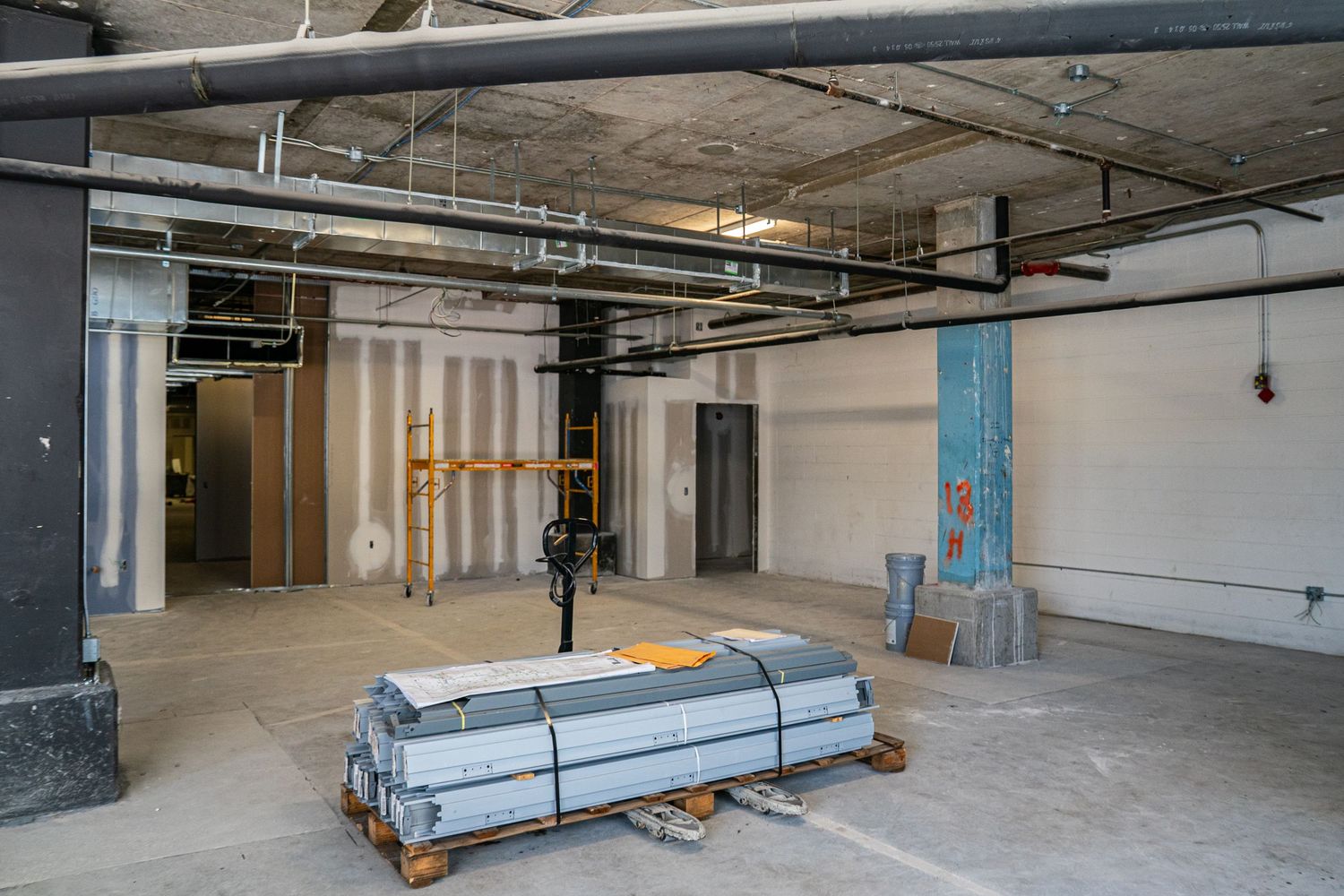 Unfinished commercial interior with HVAC ducts and construction supplies.