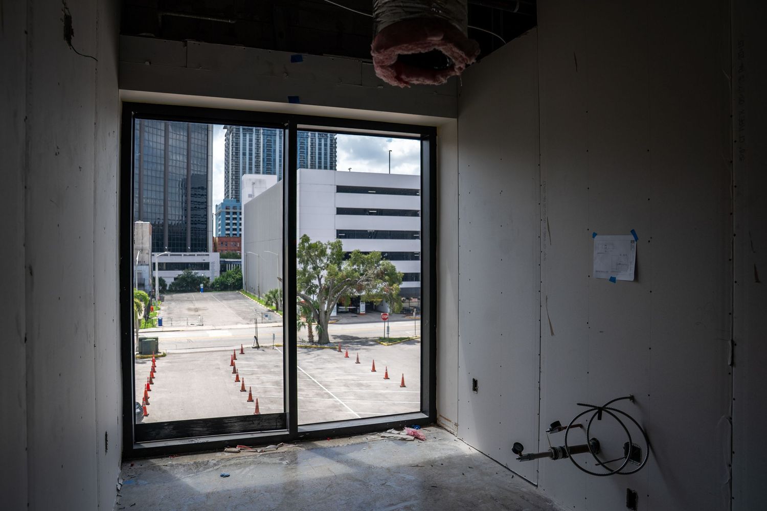 Large window view of urban buildings through an unfinished commercial space under construction.