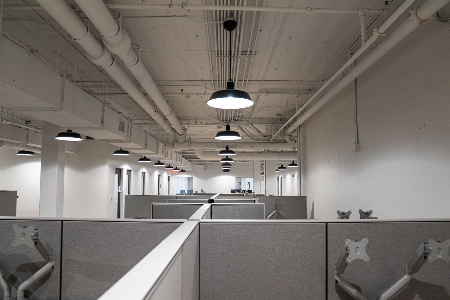 Office space with cubicle dividers and pendant lighting in industrial ceiling.