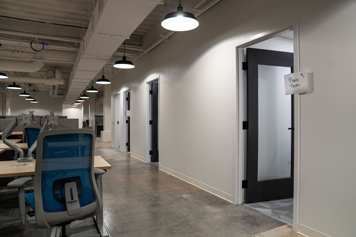Long office corridor with black pendant lights, white walls, and modular desk arrangements.