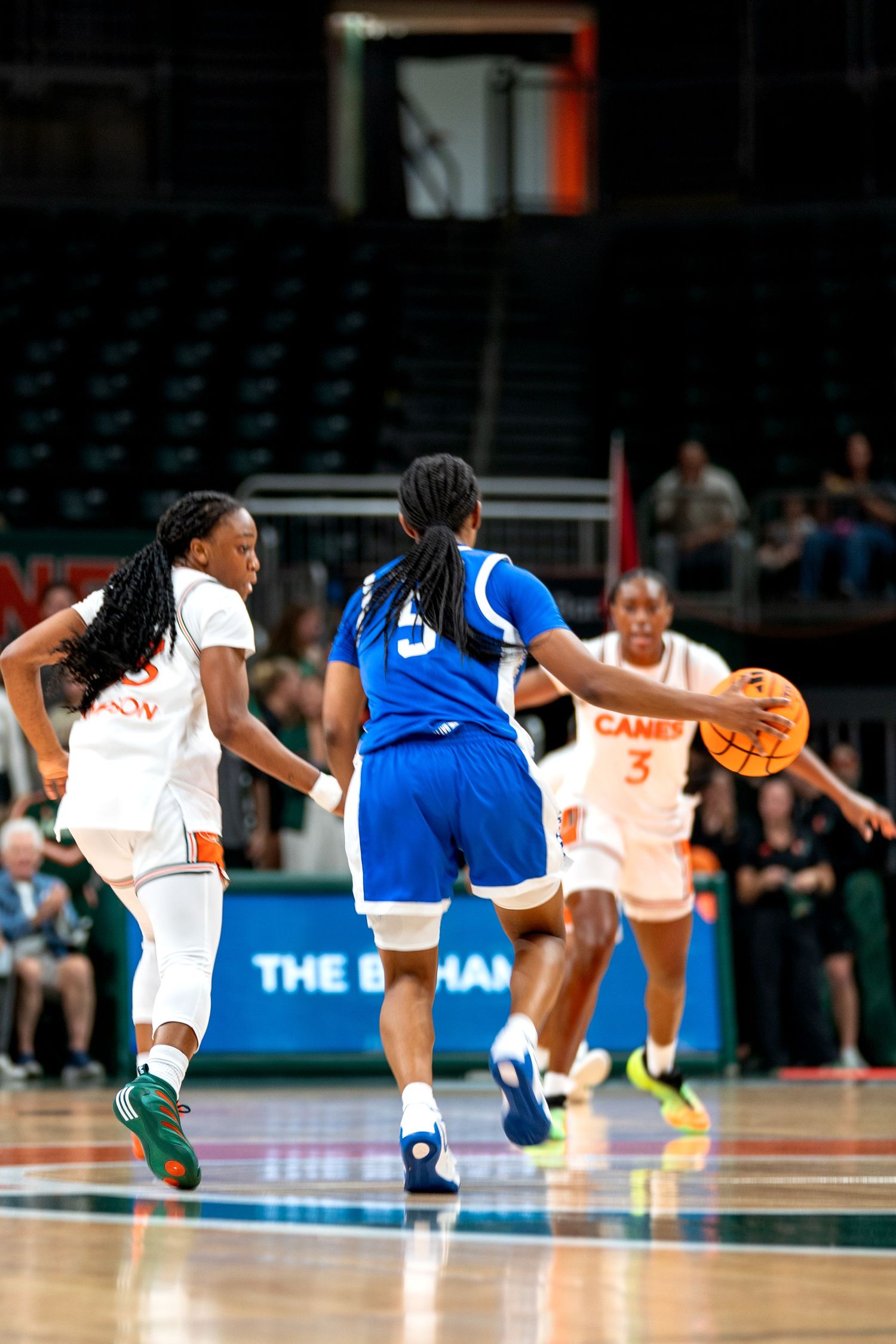 Players from opposing teams compete for ball during intense basketball game.