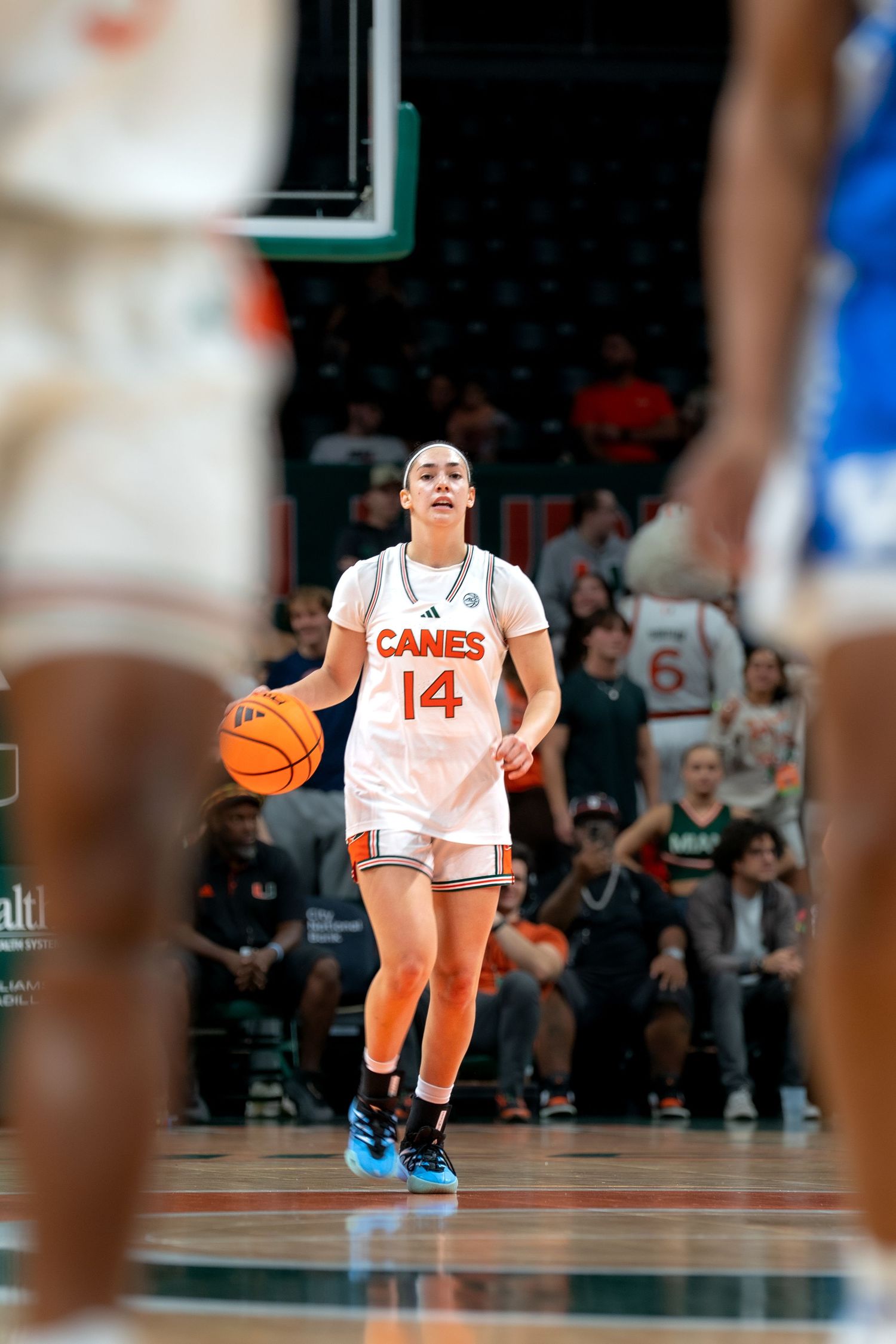 Player in white Miami Hurricanes jersey number 14 dribbles the basketball on court.