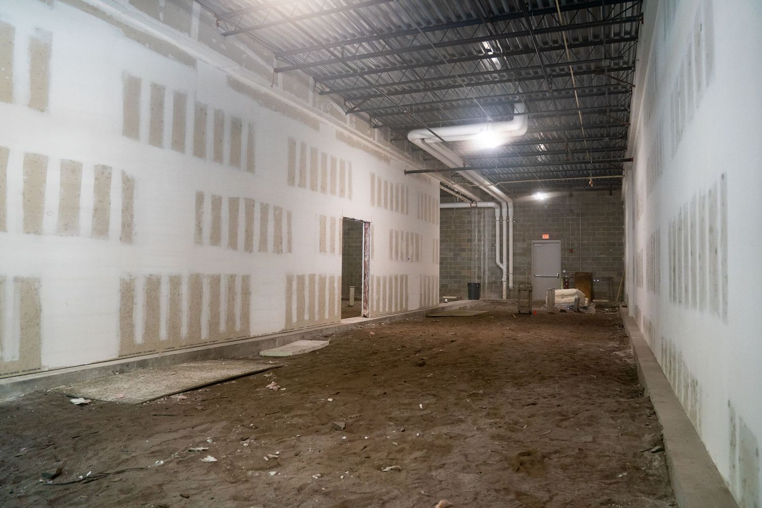 Long corridor view of commercial construction site with drywall and exposed ceiling utilities.