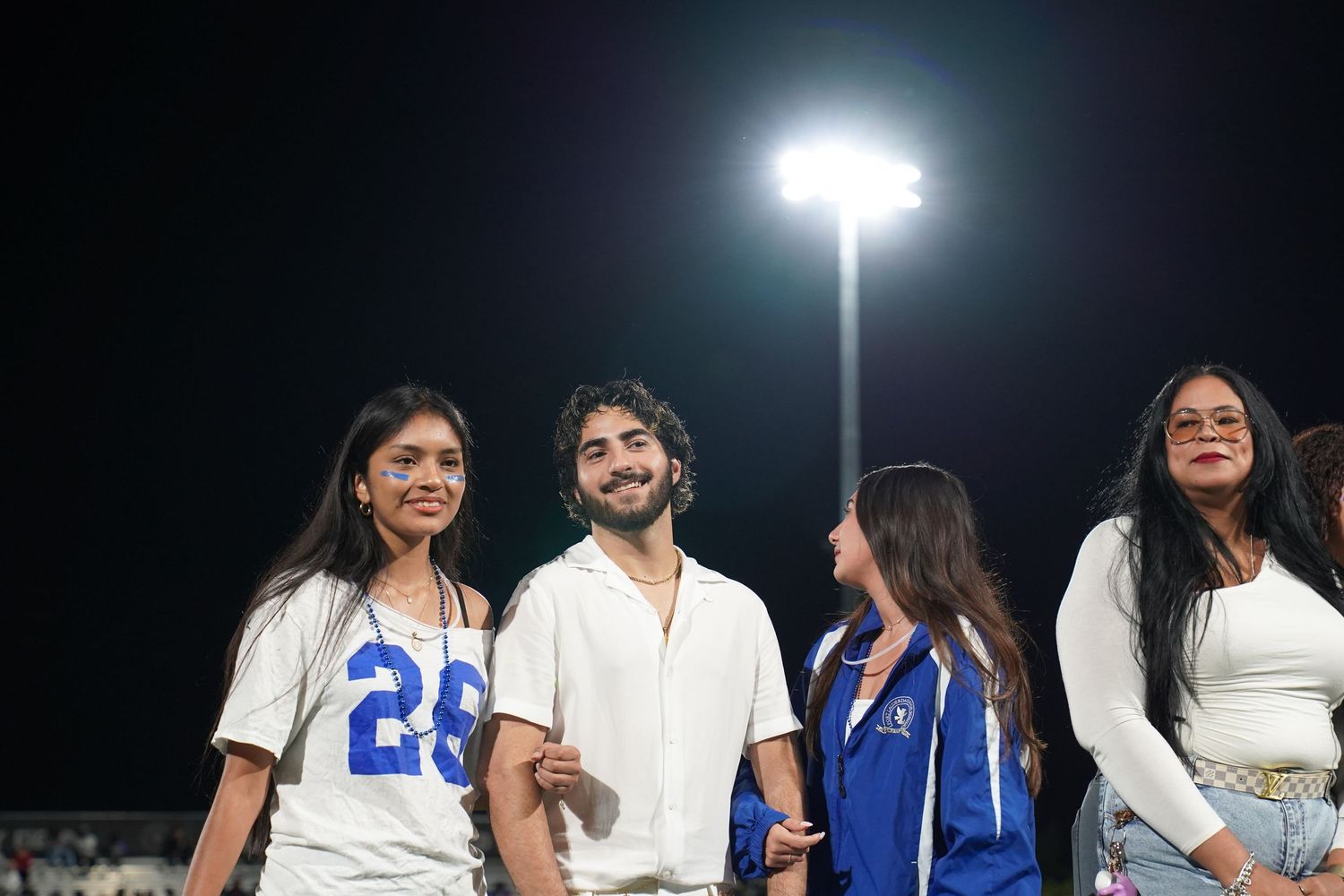Students in white and blue attire gathered under stadium lights at night.