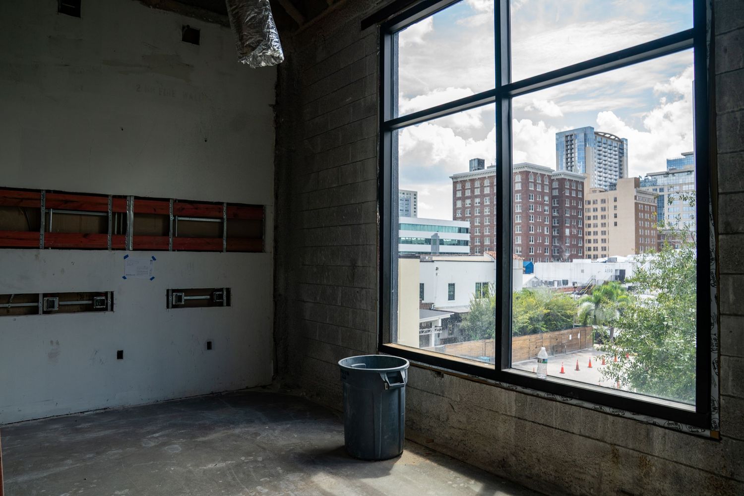 City skyline visible through large windows in an unfinished commercial space with trash bin.