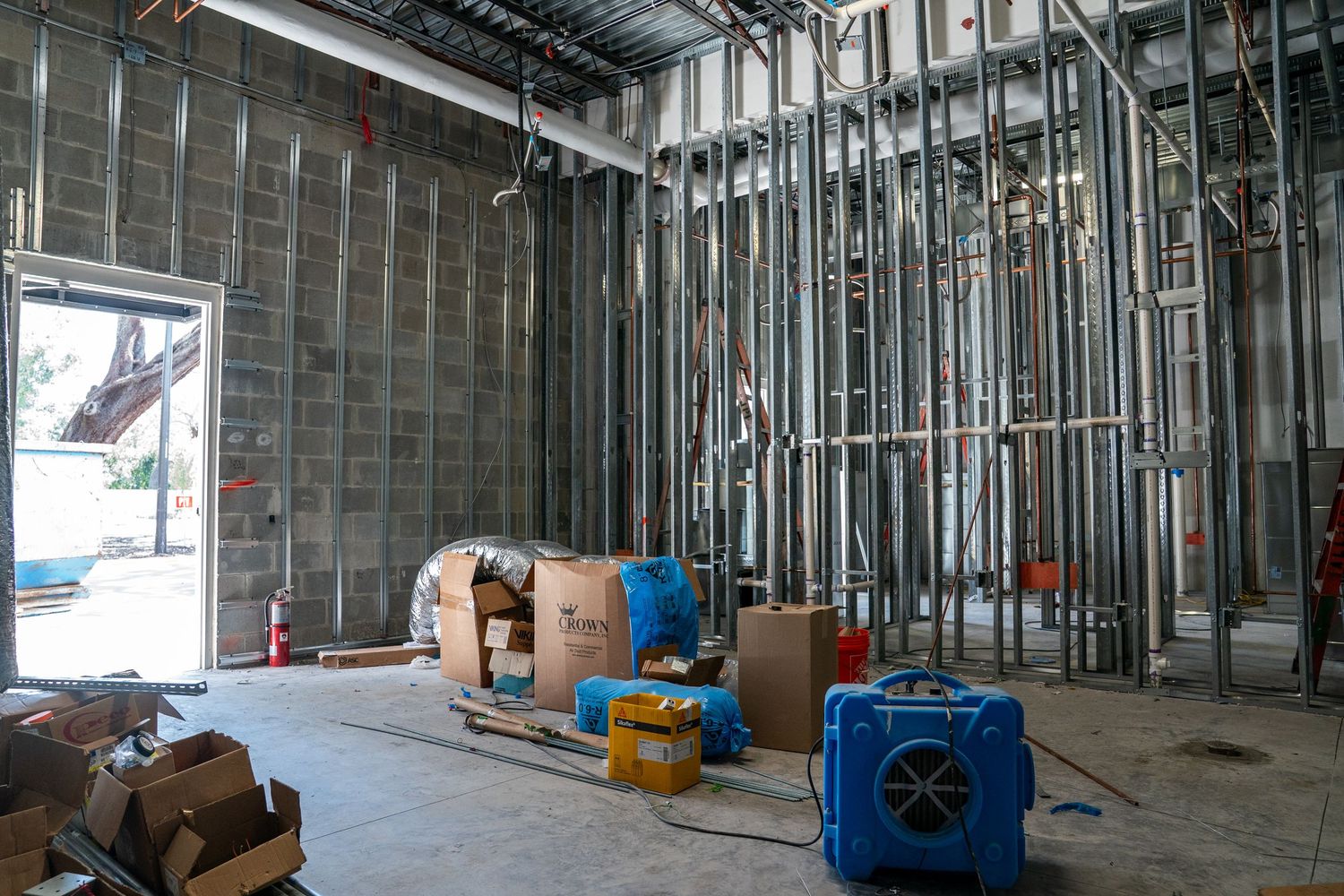Interior construction site showing metal framing and drywall installation in progress with exposed ceiling and utilities.