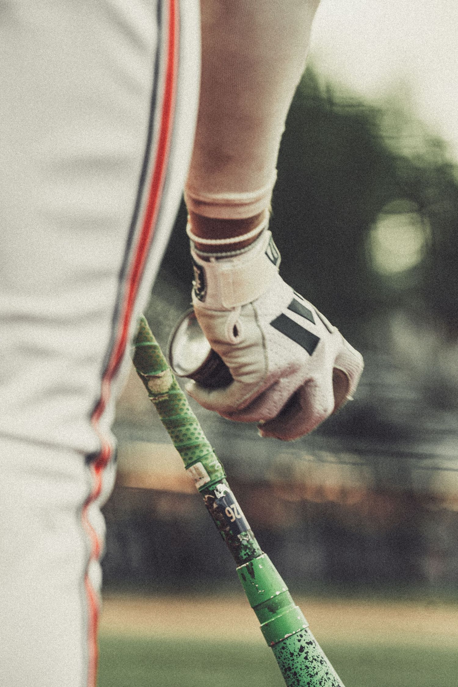 Close-up of a baseball player's gloved hand gripping a green-taped bat during a game.