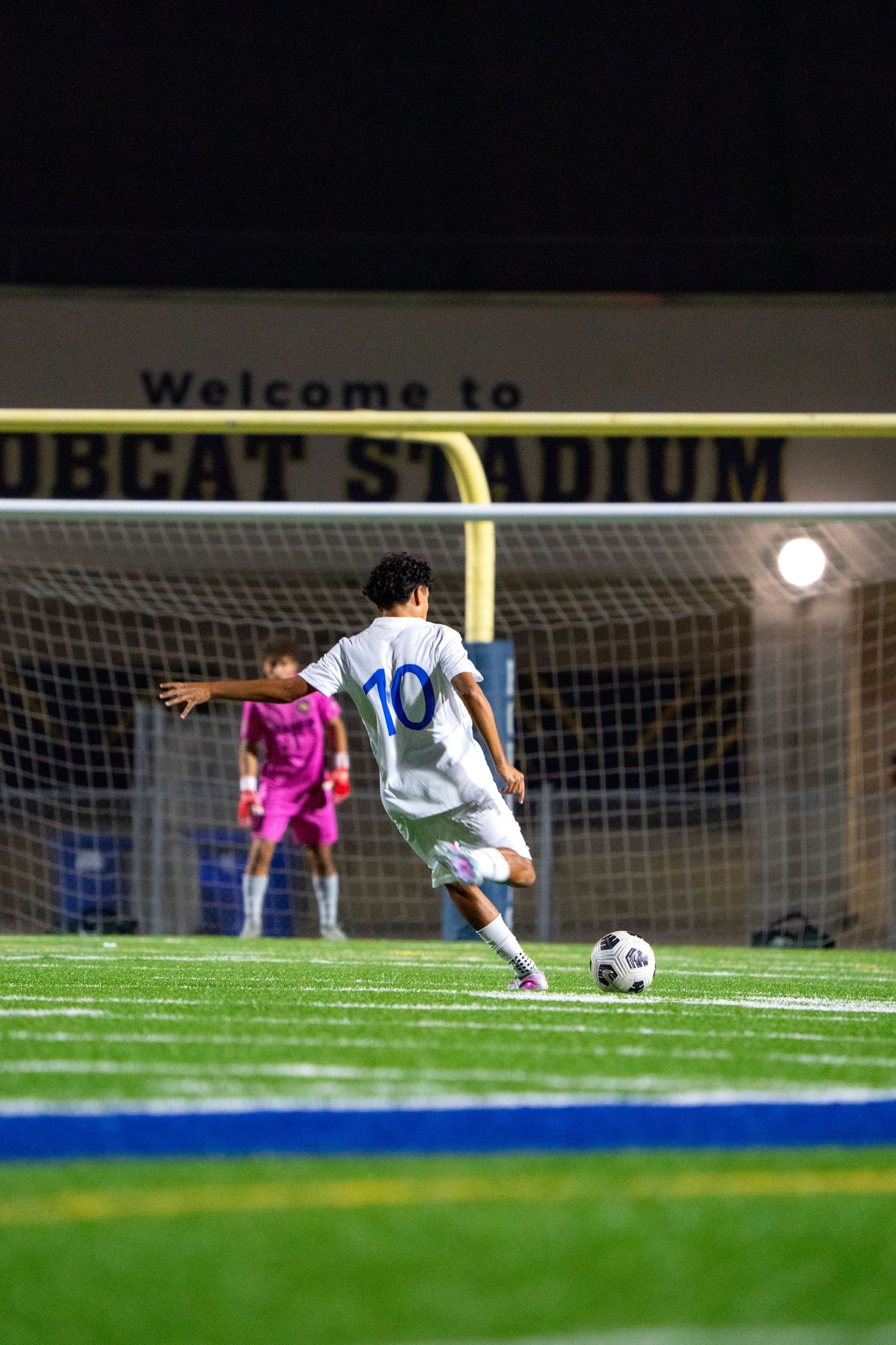 Soccer player taking a shot on goal at night with stadium lighting illuminating the field.