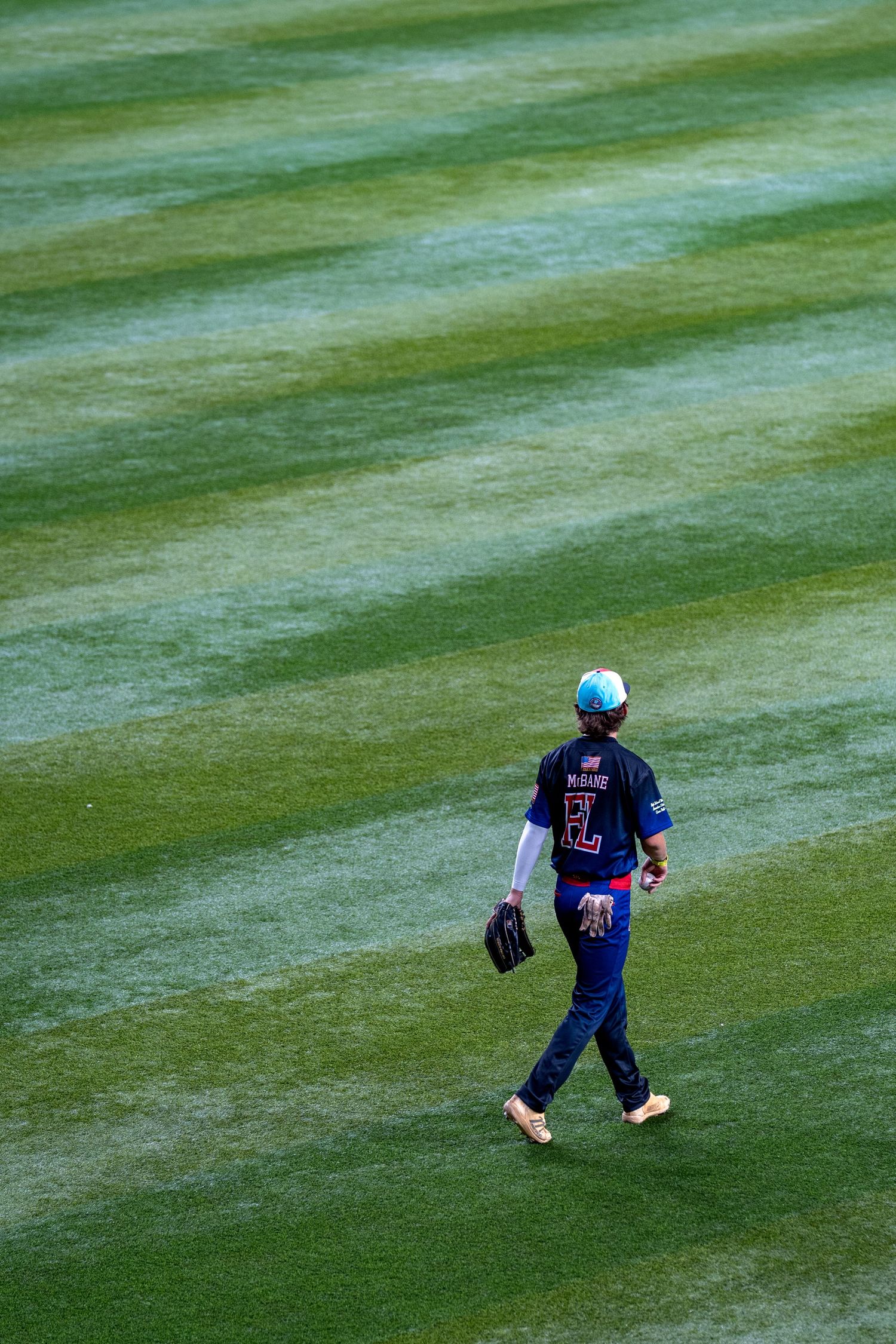 A baseball player in blue uniform walks alone across a perfectly manicured green outfield grass.