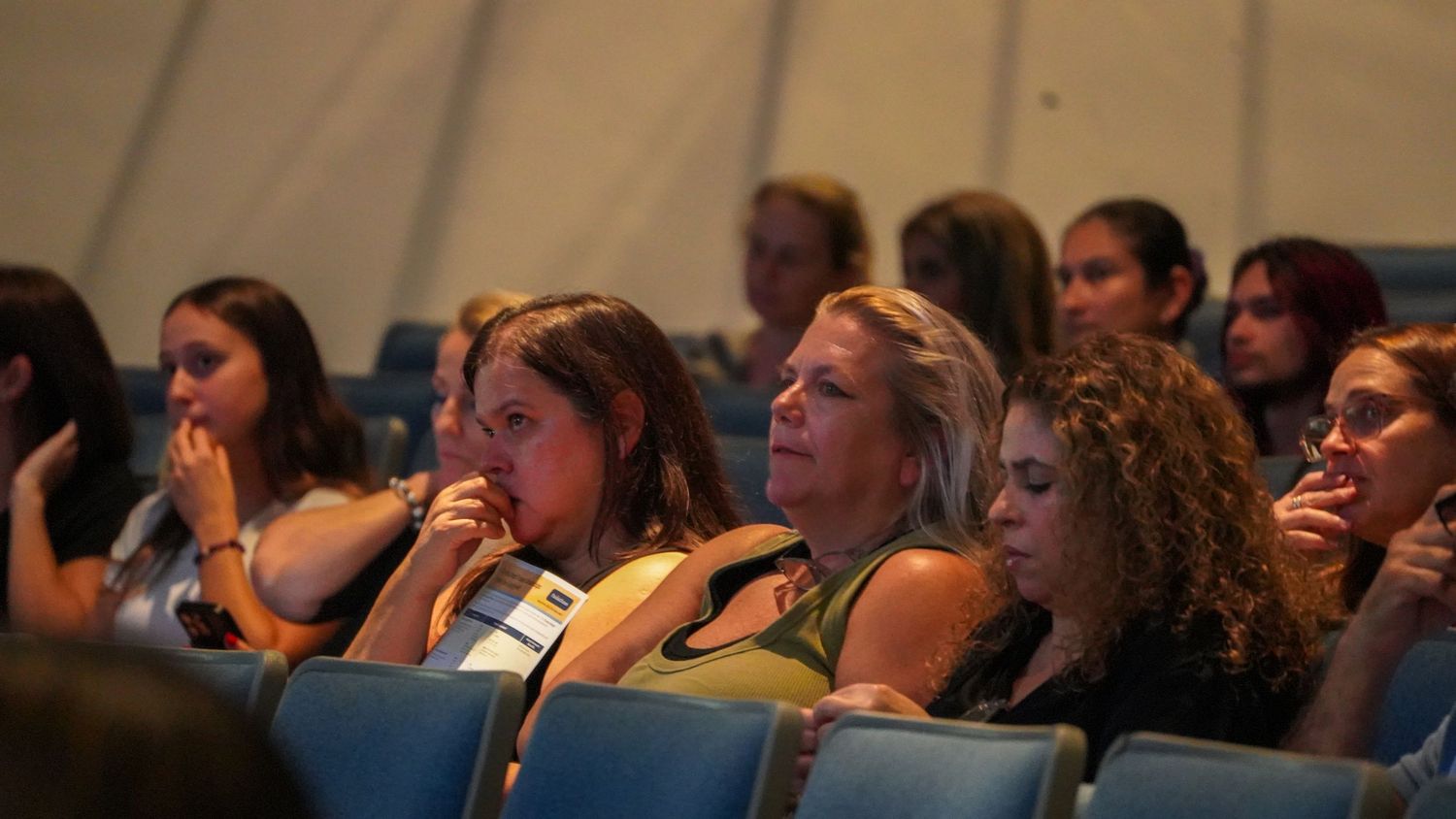 Audience members react emotionally while watching presentation in theater seating.